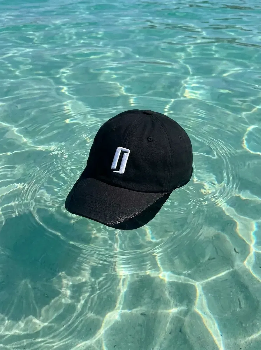 Visuel produit IA : casquette noire flottant dans une eau turquoise